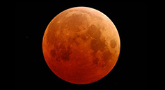 the Moon colored red and orange and appearing against the black of the night sky